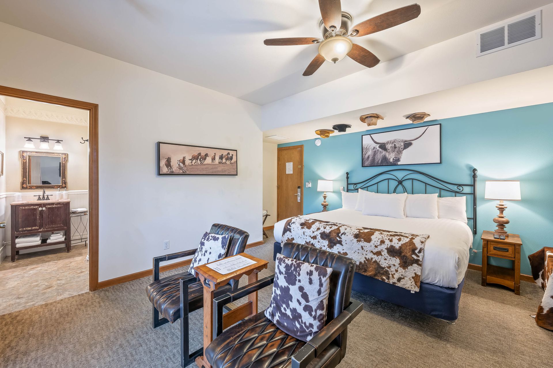 A hotel room with a king size bed , chairs and a ceiling fan.