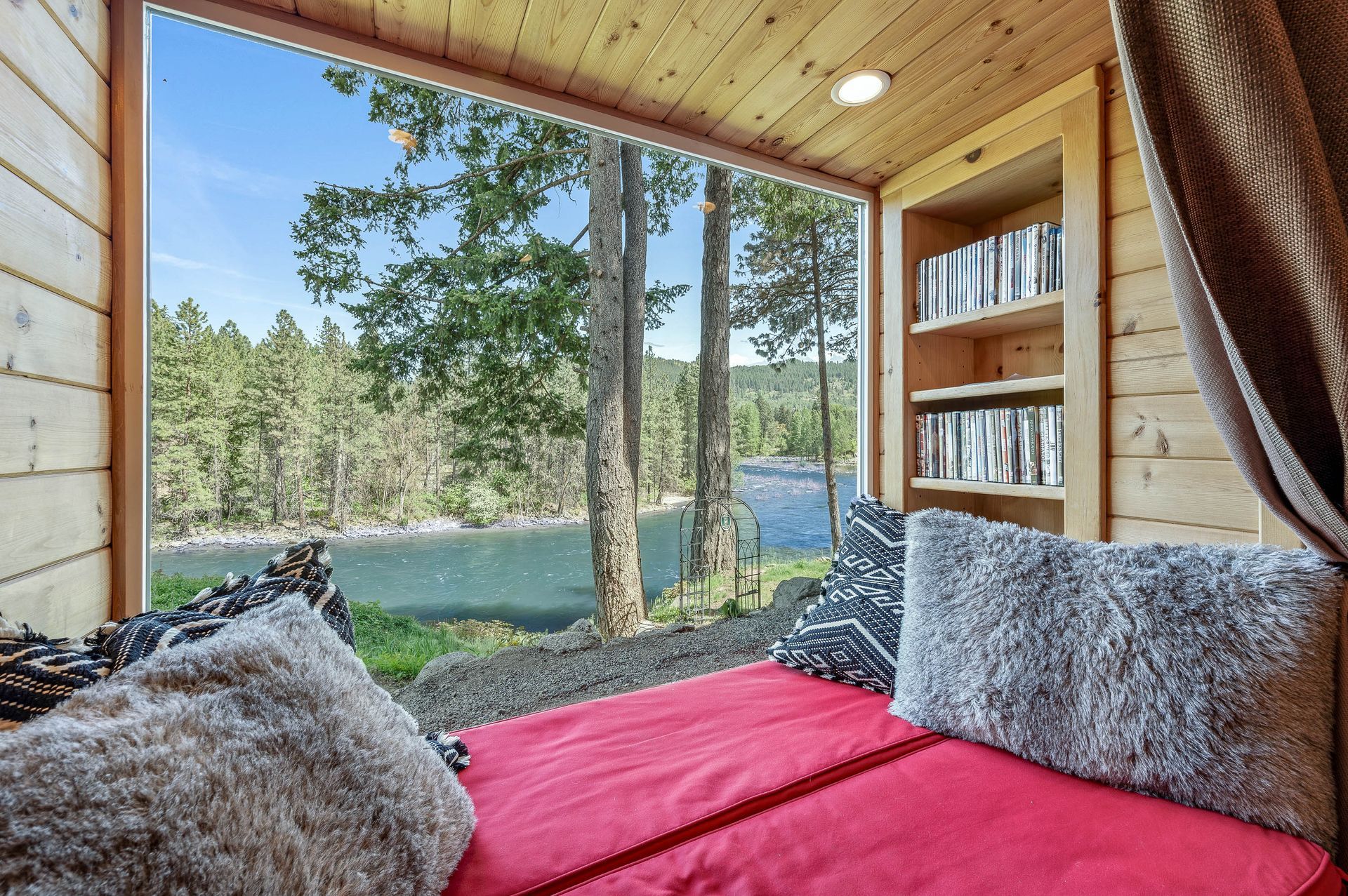 A bed is sitting in front of a window with a view of a river.