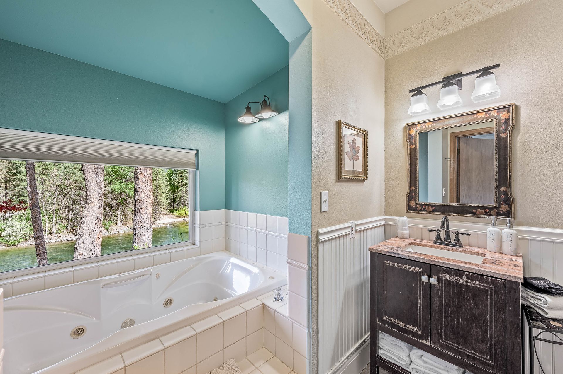 A bathroom with a jacuzzi tub , sink , mirror and window.
