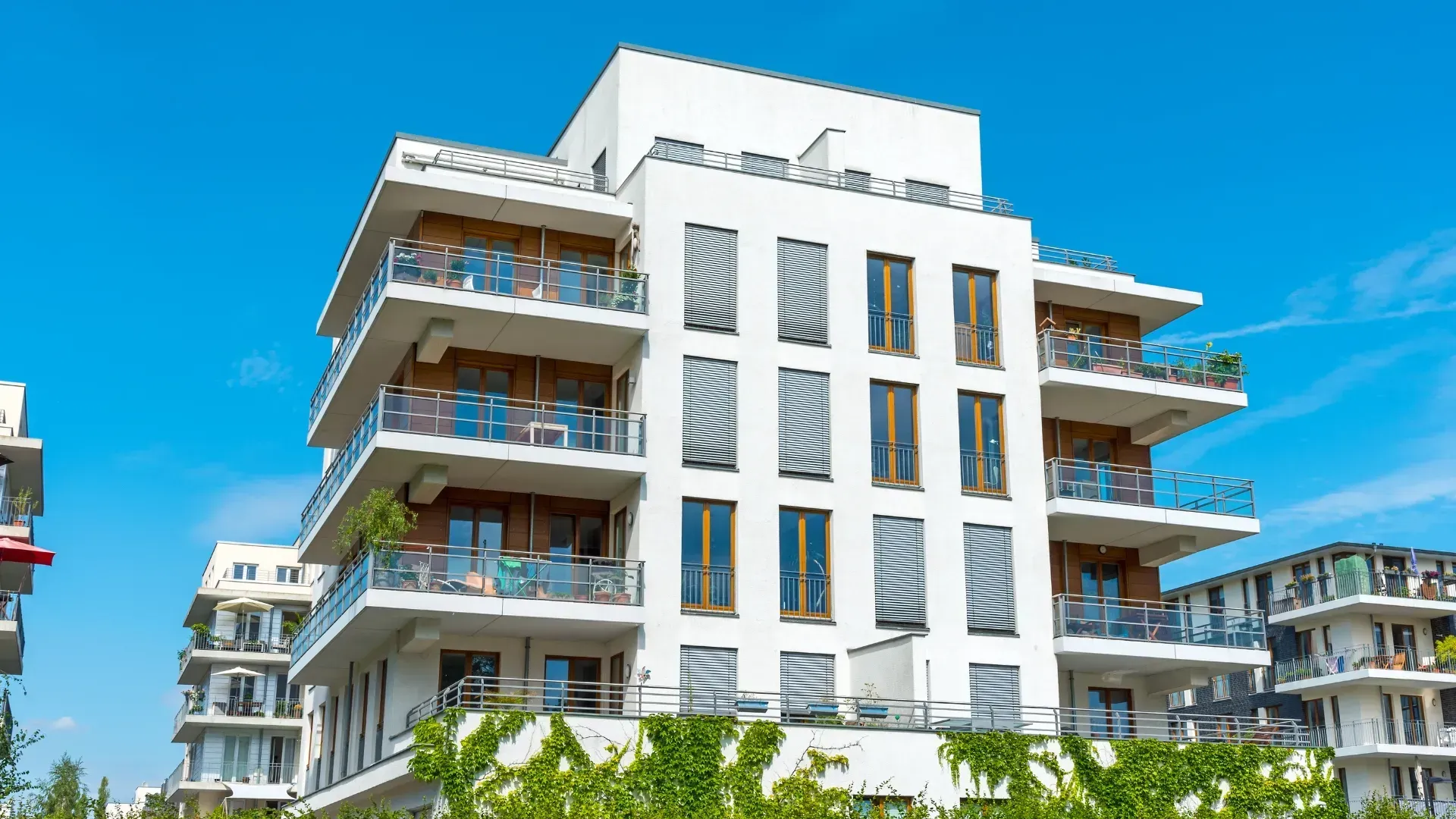 Edificio de apartamentos moderno de color blanco con balcones y un cielo azul claro.
