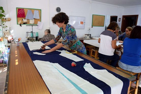 Personas midiendo y cortando tela en una gran mesa de trabajo en un taller de costura.