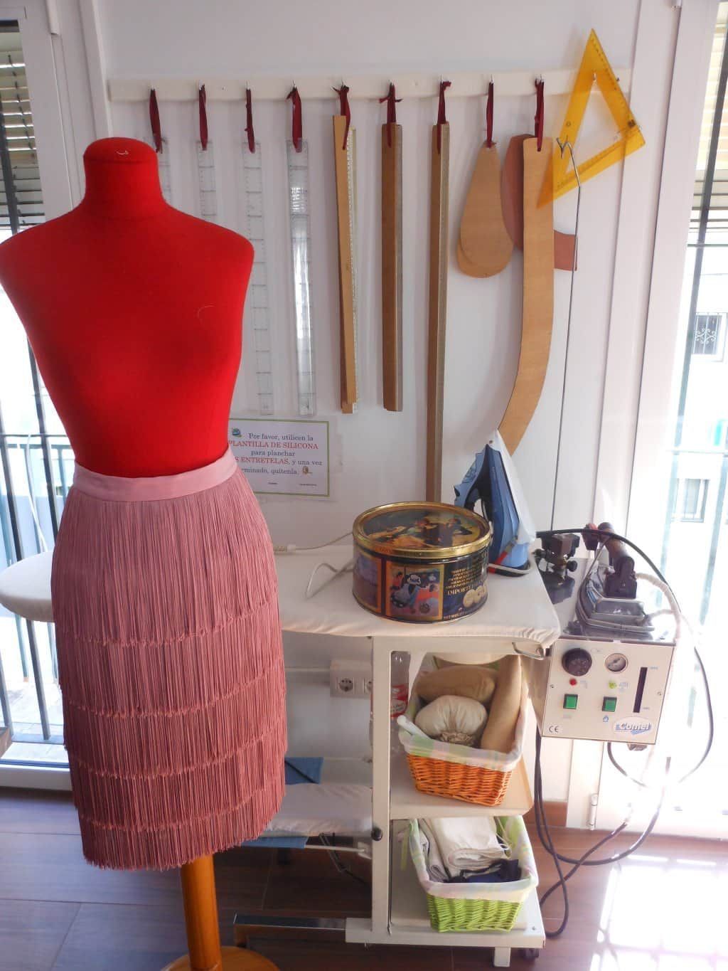 Maniquí con top rojo y falda rosa junto a herramientas y suministros de costura en un pequeño taller.