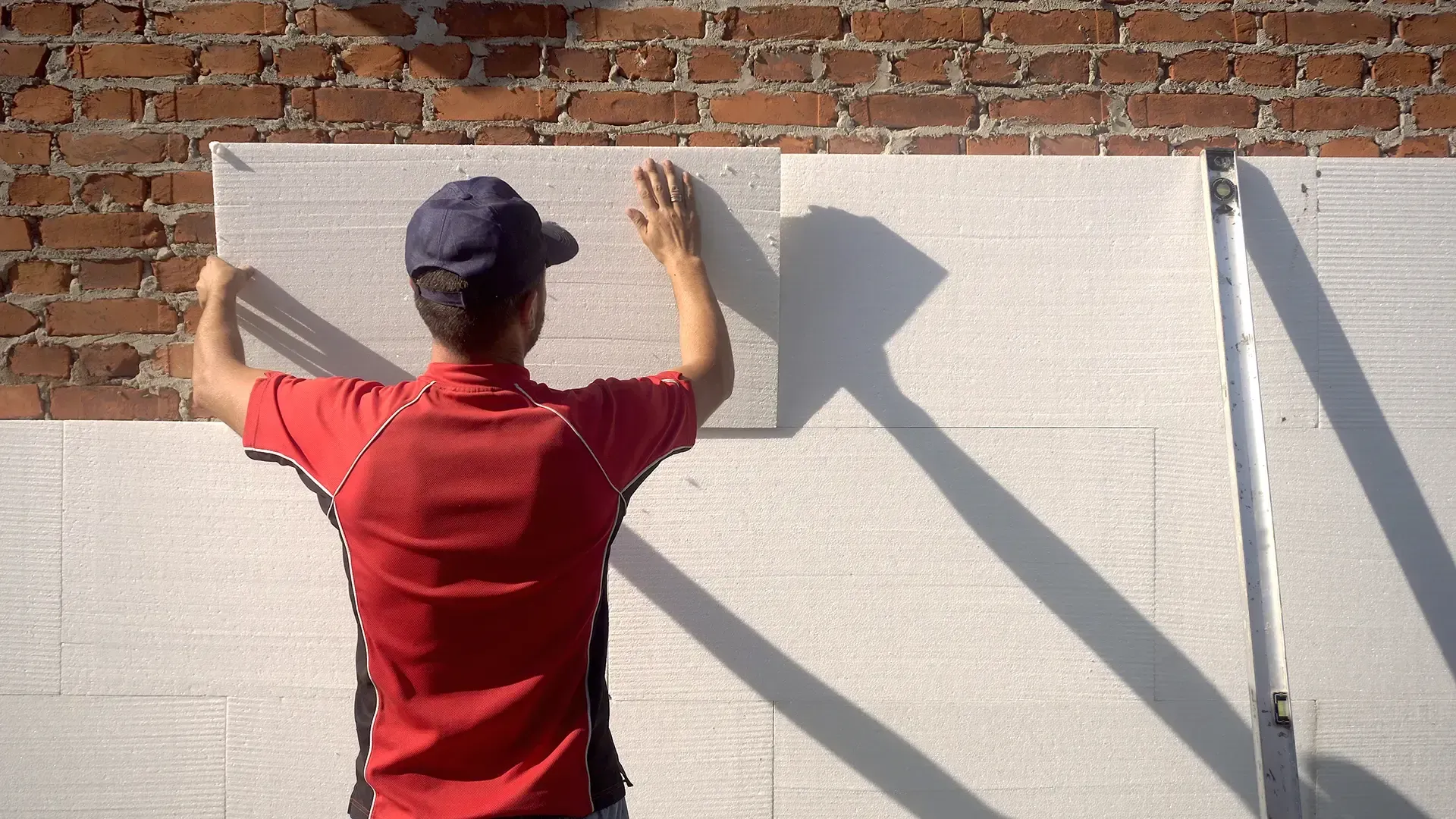 Person, die Schaumstoff-Dämmplatten an einer Ziegelwand anbringt.