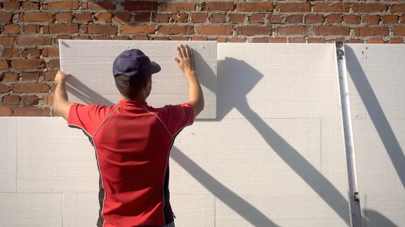 Person, die Schaumstoff-Dämmplatten an einer Ziegelwand anbringt.