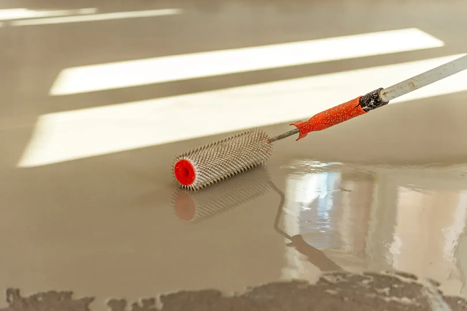 Der Boden wird mit hellgrauem Epoxidharz mittels einer Stachelwalze beschichtet.