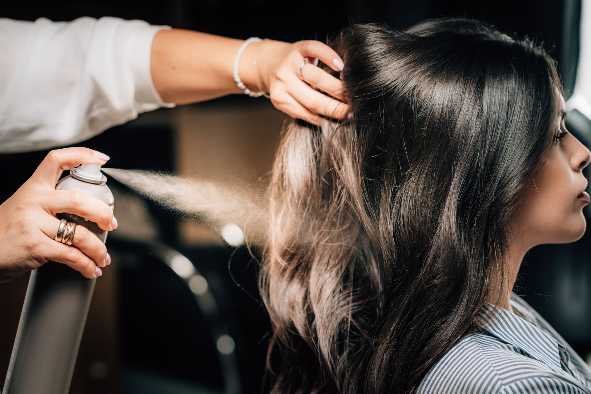 Eine Stylistin sprüht beim Stylen der Haare einer Person im Salon Haarspray auf die Haare.