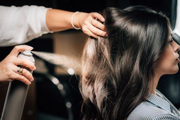 Eine Stylistin sprüht beim Stylen der Haare einer Person im Salon Haarspray auf die Haare.