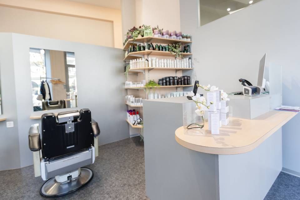 Das Interieur eines Friseursalons mit einem professionellen Stuhl vor einem Spiegel und einem Empfangstresen mit Ausstellungsregalen.