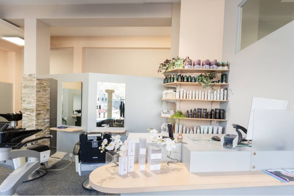Moderner Empfangsbereich eines Friseursalons mit Rezeption, Verkaufsregalen mit Haarprodukten und einem Friseurstuhl.