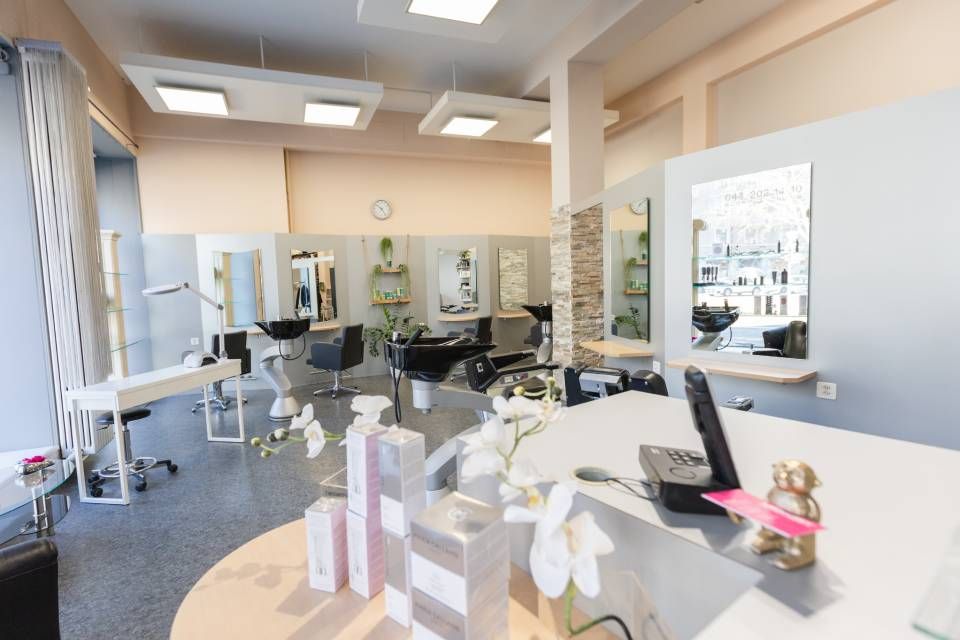 Ein modernes, helles Friseursalon-Interieur mit Frisierplätzen, Stühlen und Produktpräsentationen an einem Empfangstresen.
