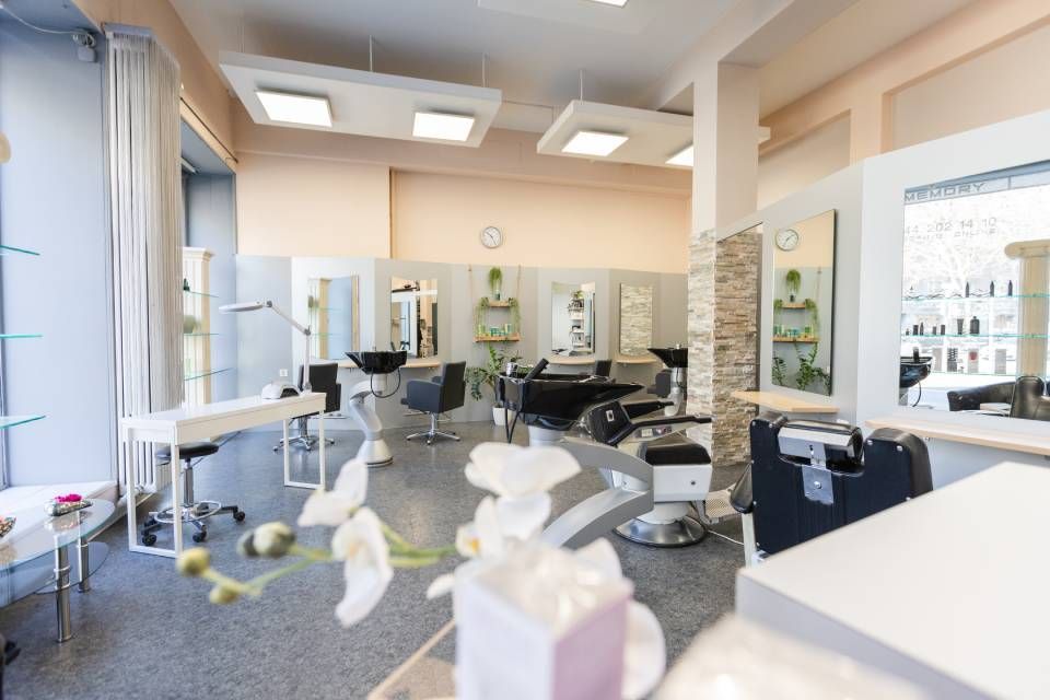 Ein modernes, helles Friseursalon-Interieur mit Friseurstühlen, Spiegeln und Arbeitsplätzen sowie weissen Wänden und Böden.