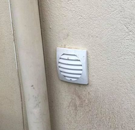 Grille d'aération fixée au mur extérieur d'une maison.