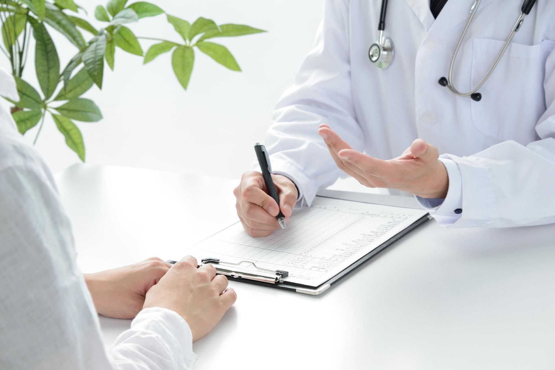 Ein Arzt spricht mit einem Patienten, während er auf einem Klemmbrett schreibt.