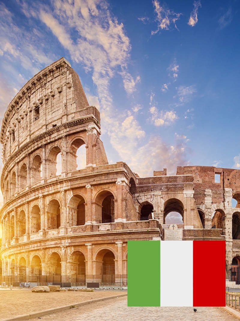 Das Kolosseum in Rom, Italien, mit der italienischen Flagge vor einem blauen Himmel. Die Sonne geht unter und verbreitet ein warmes Licht.