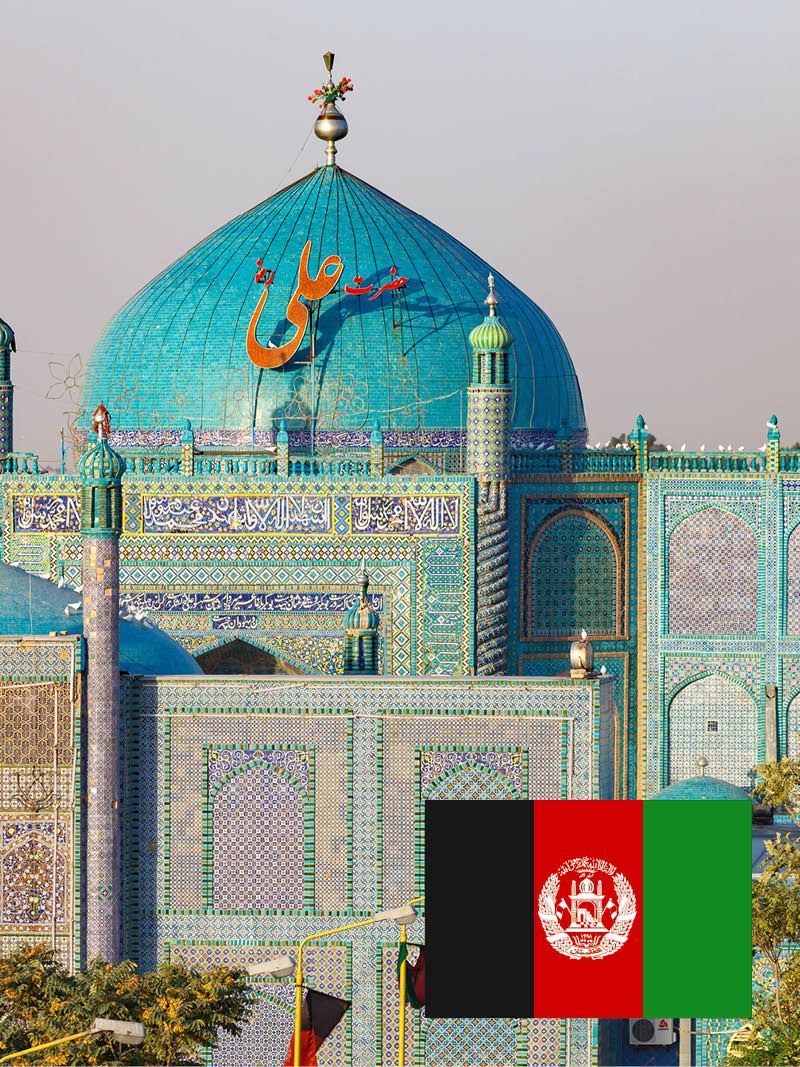 Blau geflieste Moschee mit großer Kuppel in Afghanistan; afghanische Flagge im Vordergrund.