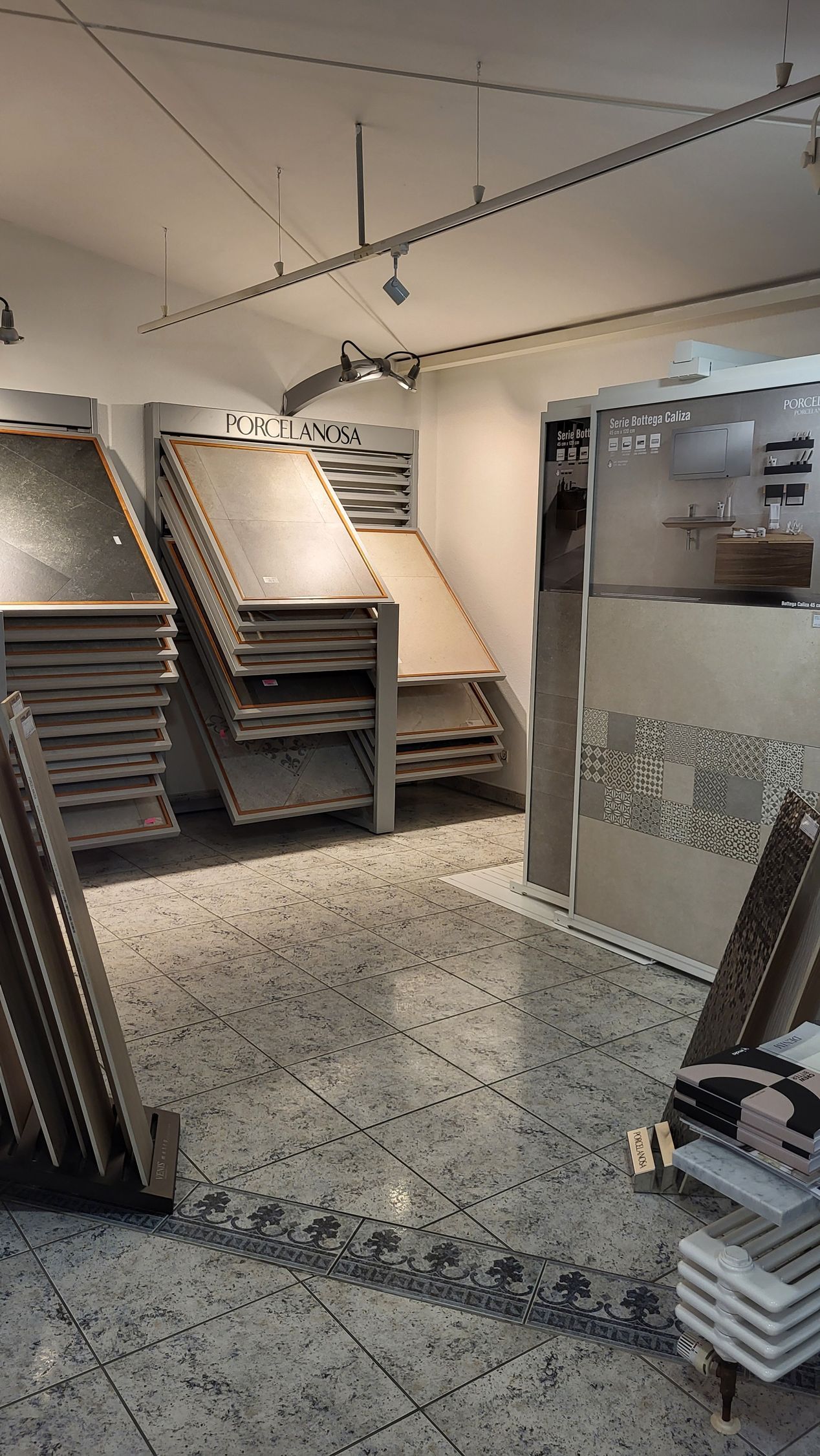 Verschiedene Fliesenmuster werden ausgestellt. Auf dem Boden ist ein Fliesenmuster in Marmoroptik und Verzierungen.