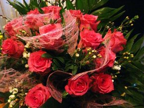 Strauß roter Rosen, umhüllt von rosa Netzstoff, mit grünem Laub und weißen Knospen