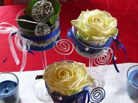 Dekorative, mit Bändern umwickelte Kerzenhalter mit rosenförmigen Blüten auf einer roten Tischdecke