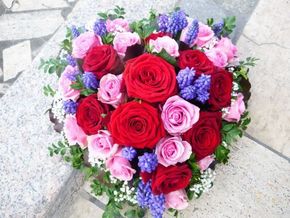 Herzförmiger Strauß aus roten, rosa und violetten Rosen auf hellem Steingrund