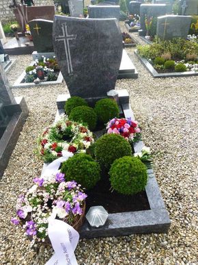 Grabstein auf einem Friedhof mit frischen Blumenarrangements und gestutzten grünen Sträuchern.