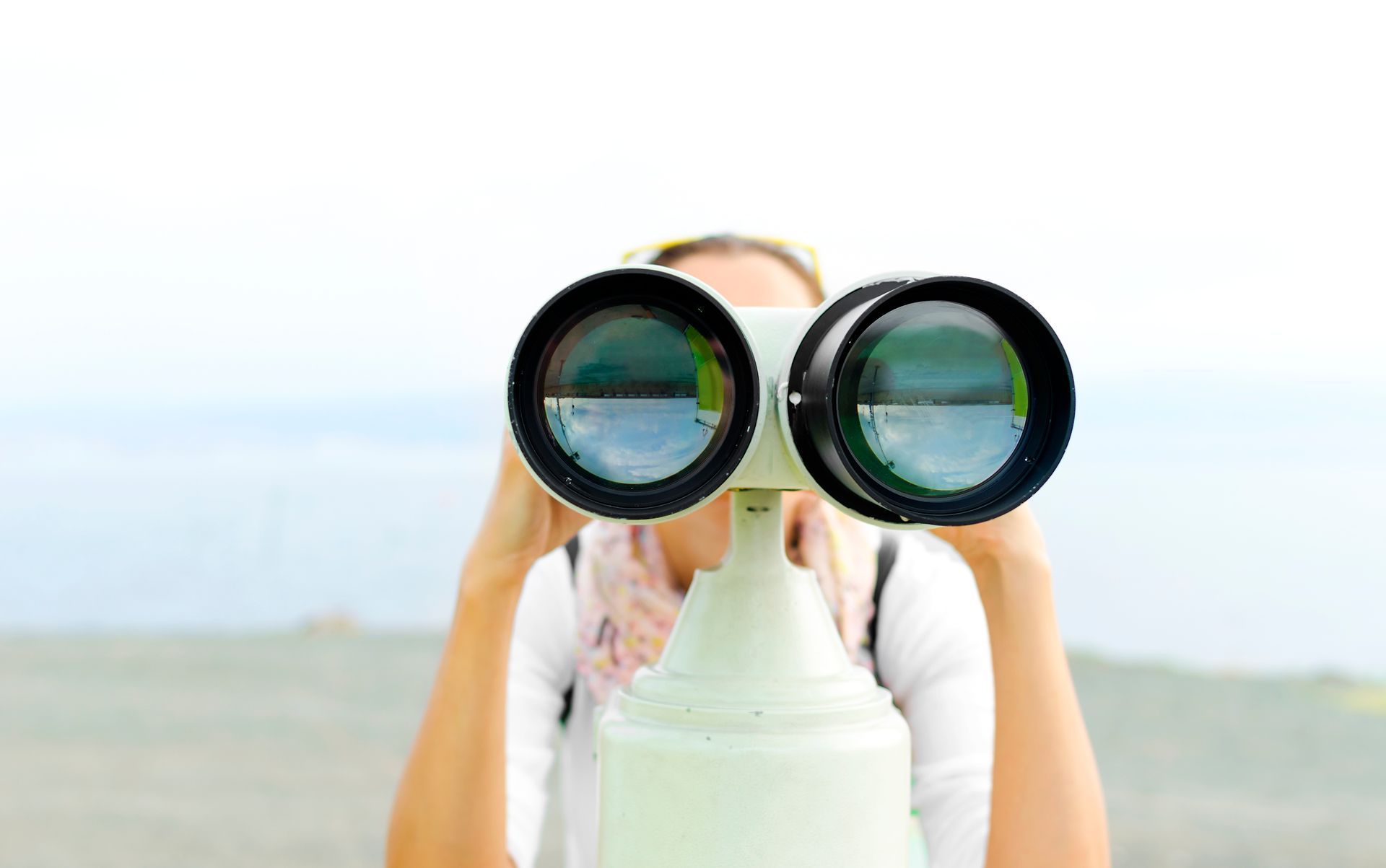 Eine Person schaut im Freien durch ein auf einem Sockel montiertes, münzbetriebenes Teleskop; der Hintergrund ist unscharf.