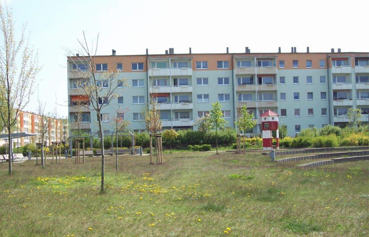 Ein rot-weiß gestreiftes Leuchtturmmodell in einem Park vor einem mehrstöckigen Wohnhaus.