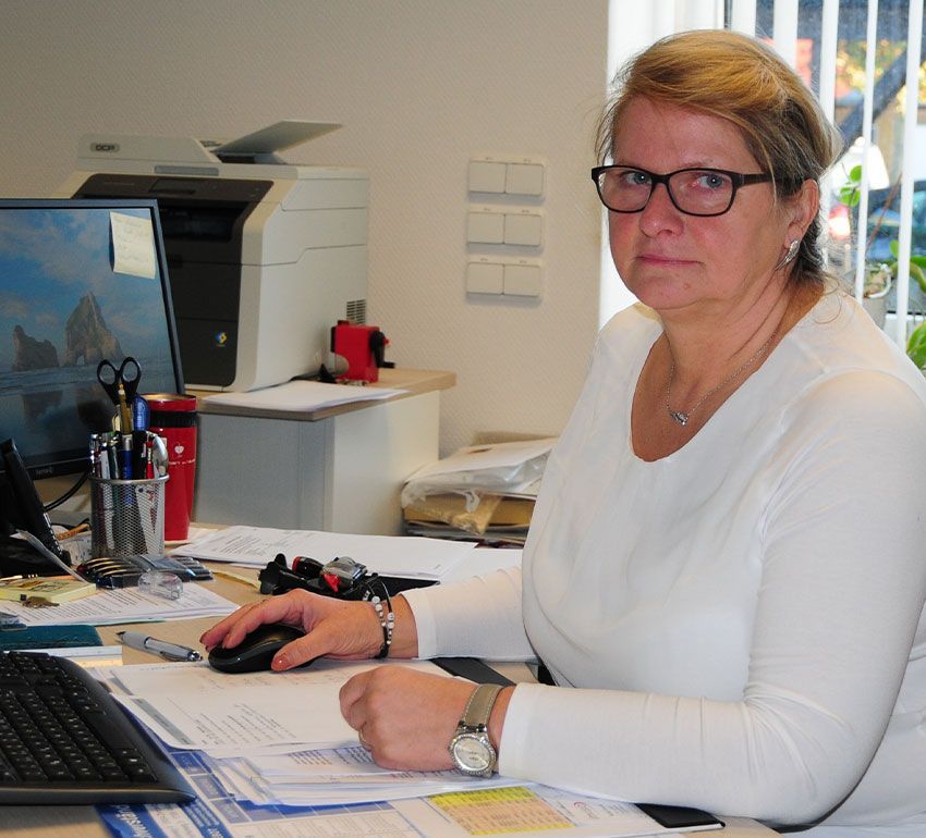 Ein Berufstätiger sitzt in einem Büro an einem Schreibtisch mit Computer, Maus und Dokumenten.