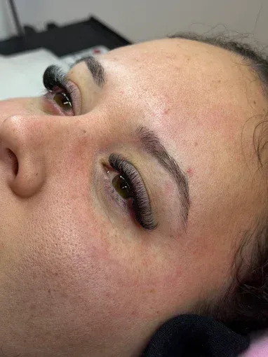 Mano con uñas largas y rosas bien cuidadas y detalles brillantes, apoyada sobre una superficie suave y peluda de color rosa.
