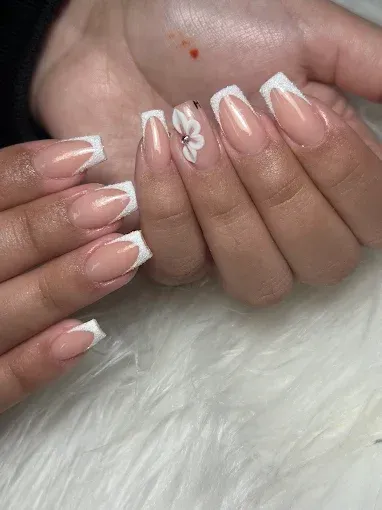 Manicura francesa con puntas blancas y un pequeño detalle de flor blanca sobre uñas nude brillantes.
