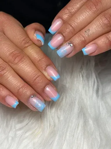 Manos con uñas pintadas en tonos rosa pastel y azul, con la punta francesa, descansando sobre piel blanca.