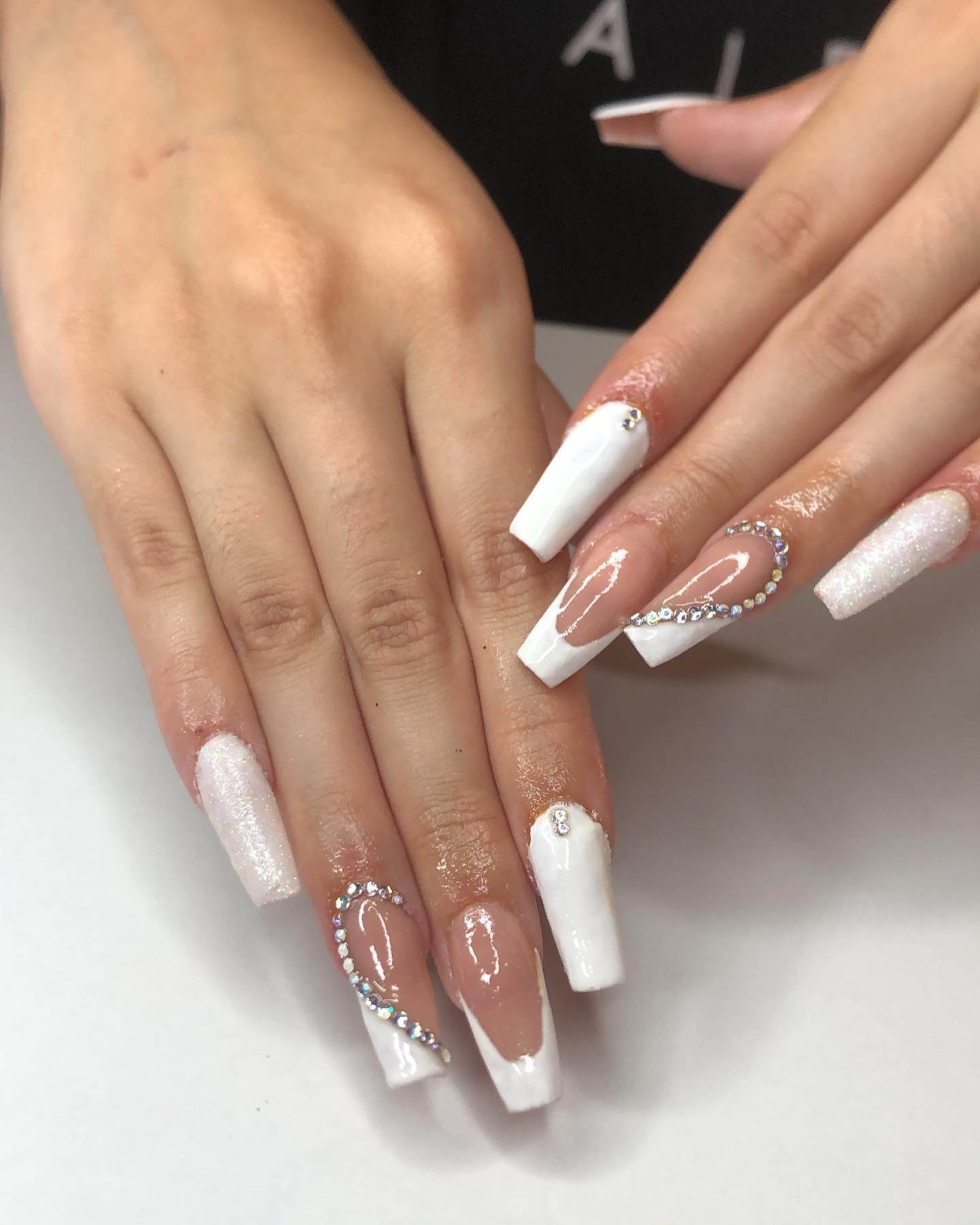 Primer plano de manos bien cuidadas con uñas acrílicas largas de color nude y uñas decoradas con flores brillantes.