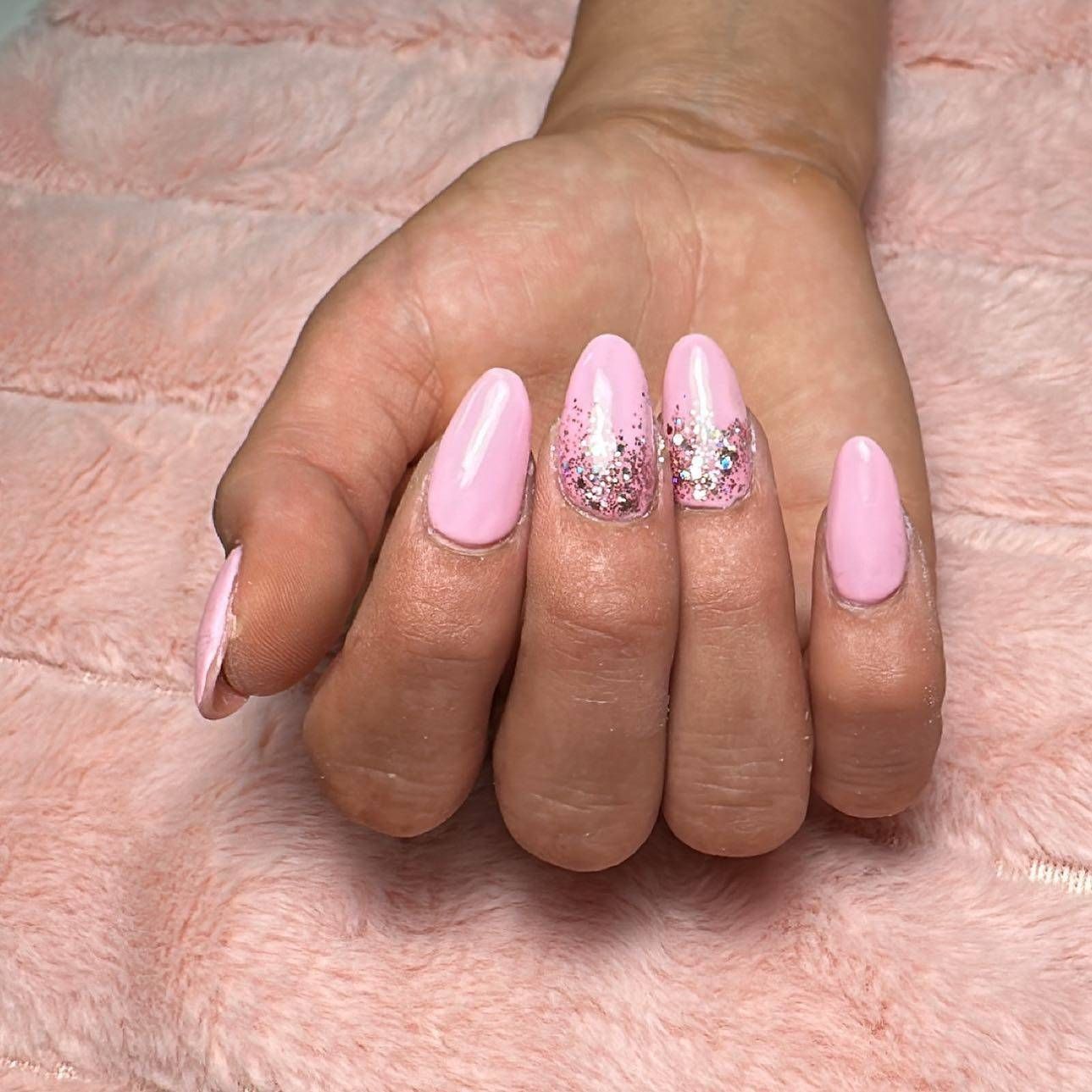 Mano con uñas largas y rosas bien cuidadas y detalles brillantes, apoyada sobre una superficie suave y peluda de color rosa.
