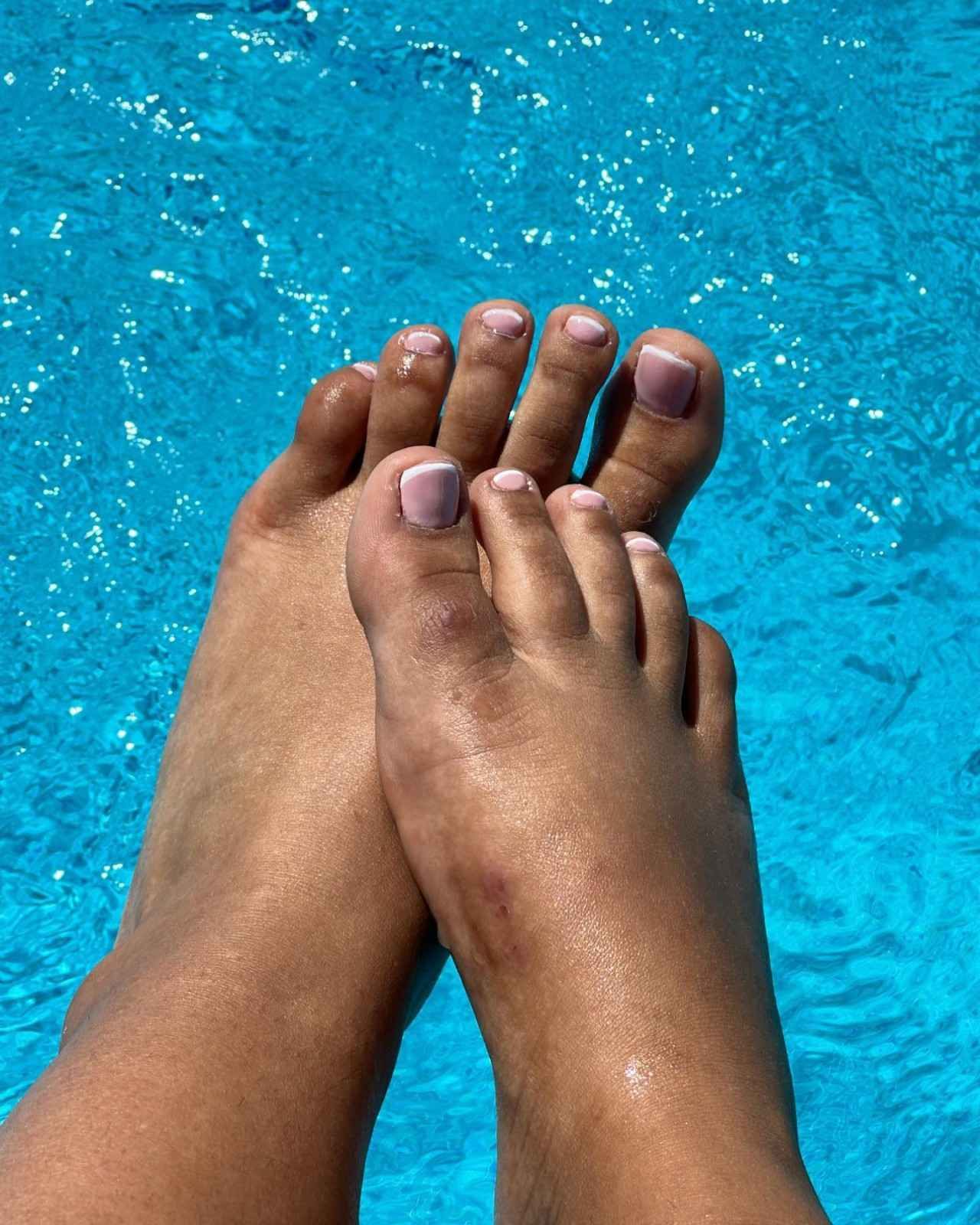 Manicura francesa con puntas blancas y un pequeño detalle de flor blanca sobre uñas nude brillantes.