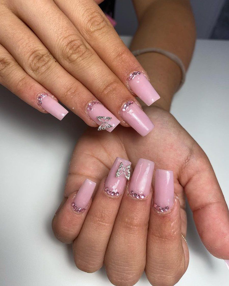 Primer plano de manos bien cuidadas con uñas acrílicas largas de color nude y uñas decoradas con flores brillantes.