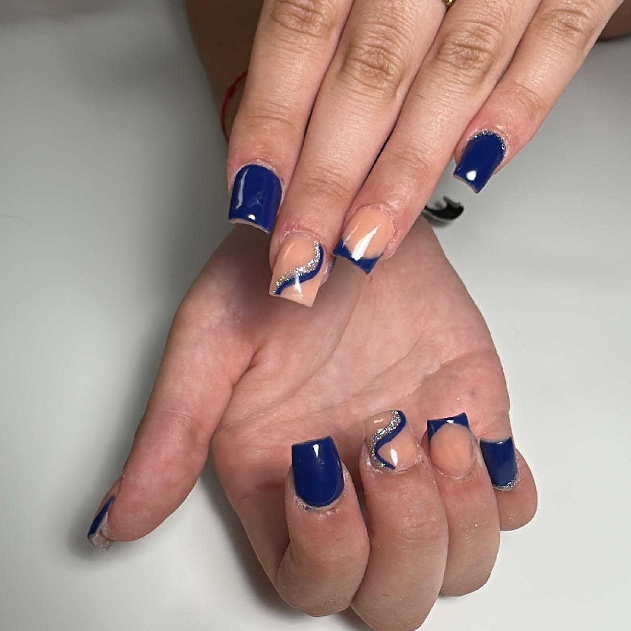 Manicura francesa con puntas blancas y un pequeño detalle de flor blanca sobre uñas nude brillantes.