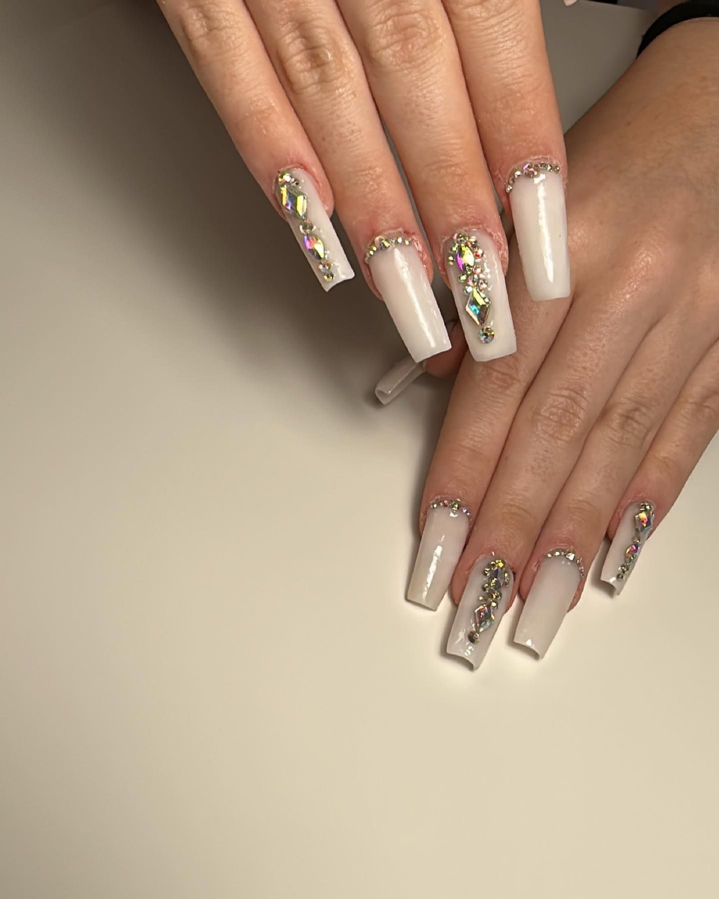 Primer plano de manos bien cuidadas con uñas acrílicas largas de color nude y uñas decoradas con flores brillantes.