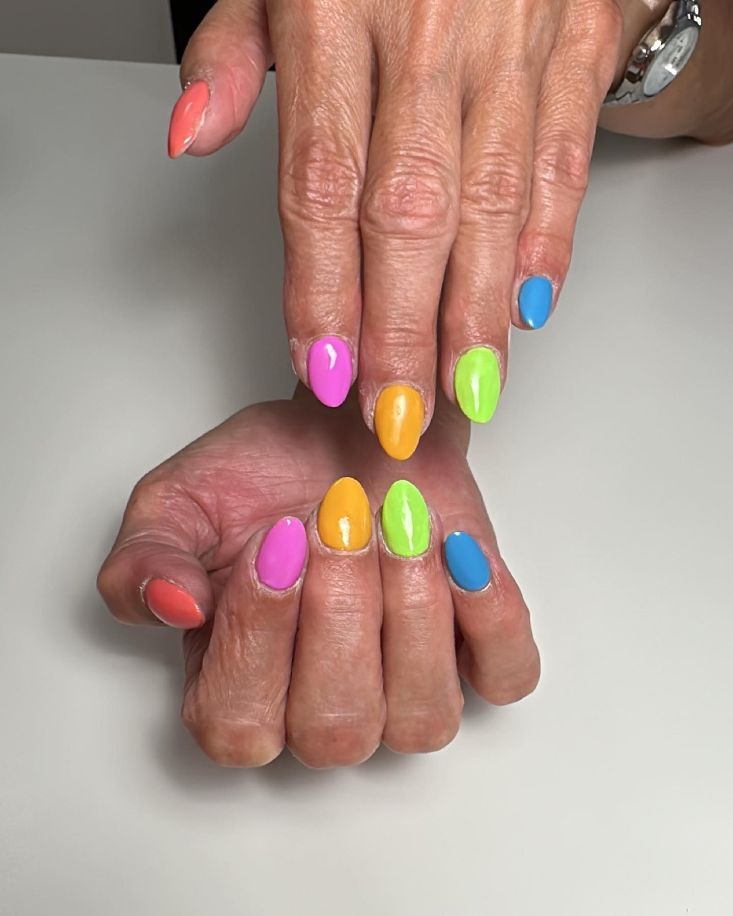 Manos con uñas pintadas de colores brillantes y bien cuidadas, mostradas sobre un fondo blanco.