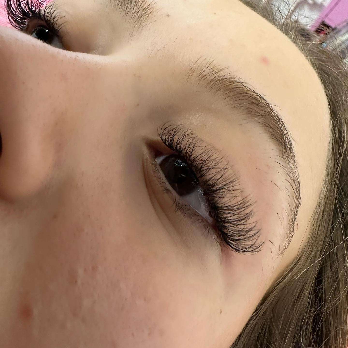 Mano con uñas largas y rosas bien cuidadas y detalles brillantes, apoyada sobre una superficie suave y peluda de color rosa.