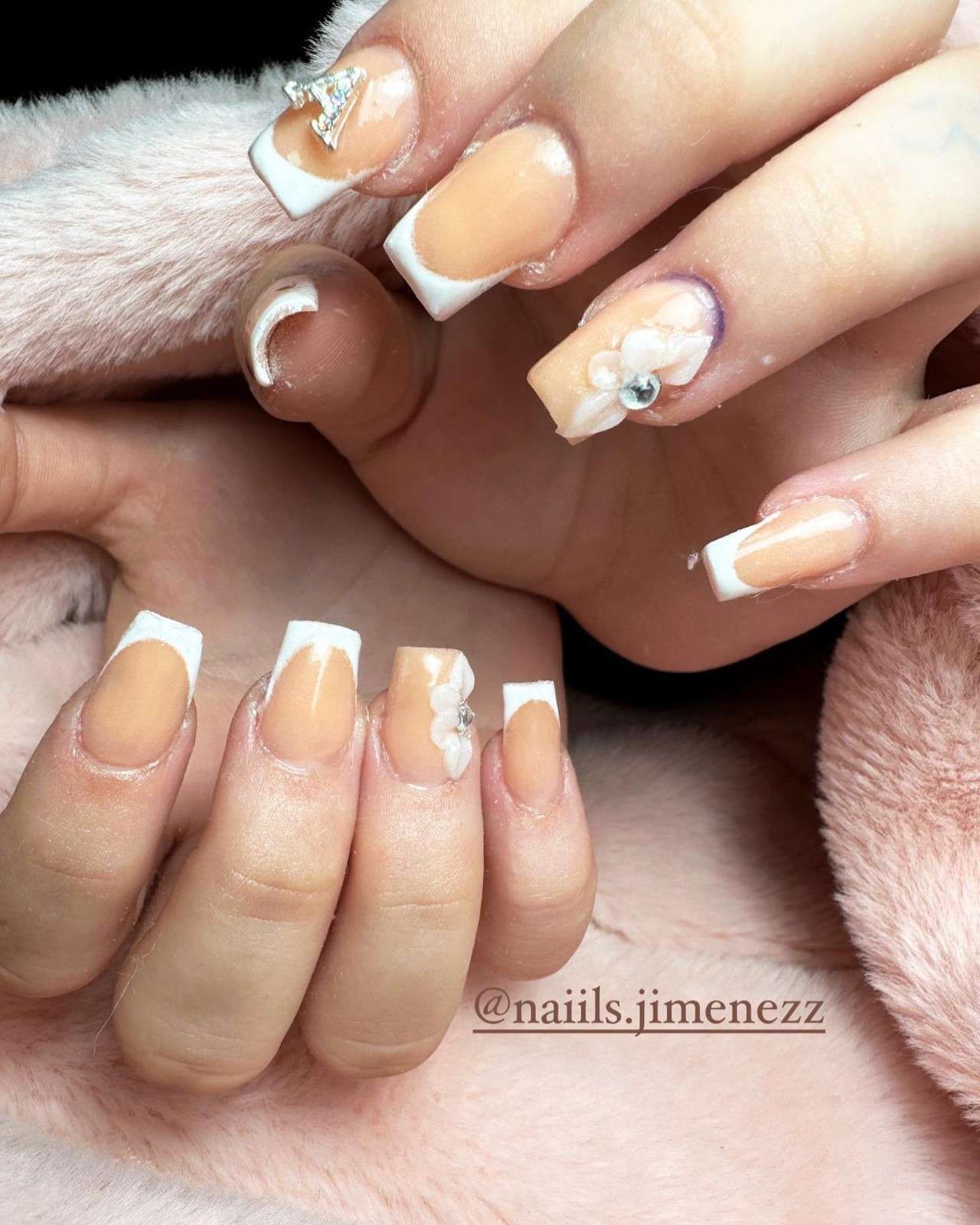 Manicura francesa con puntas blancas y un pequeño detalle de flor blanca sobre uñas nude brillantes.