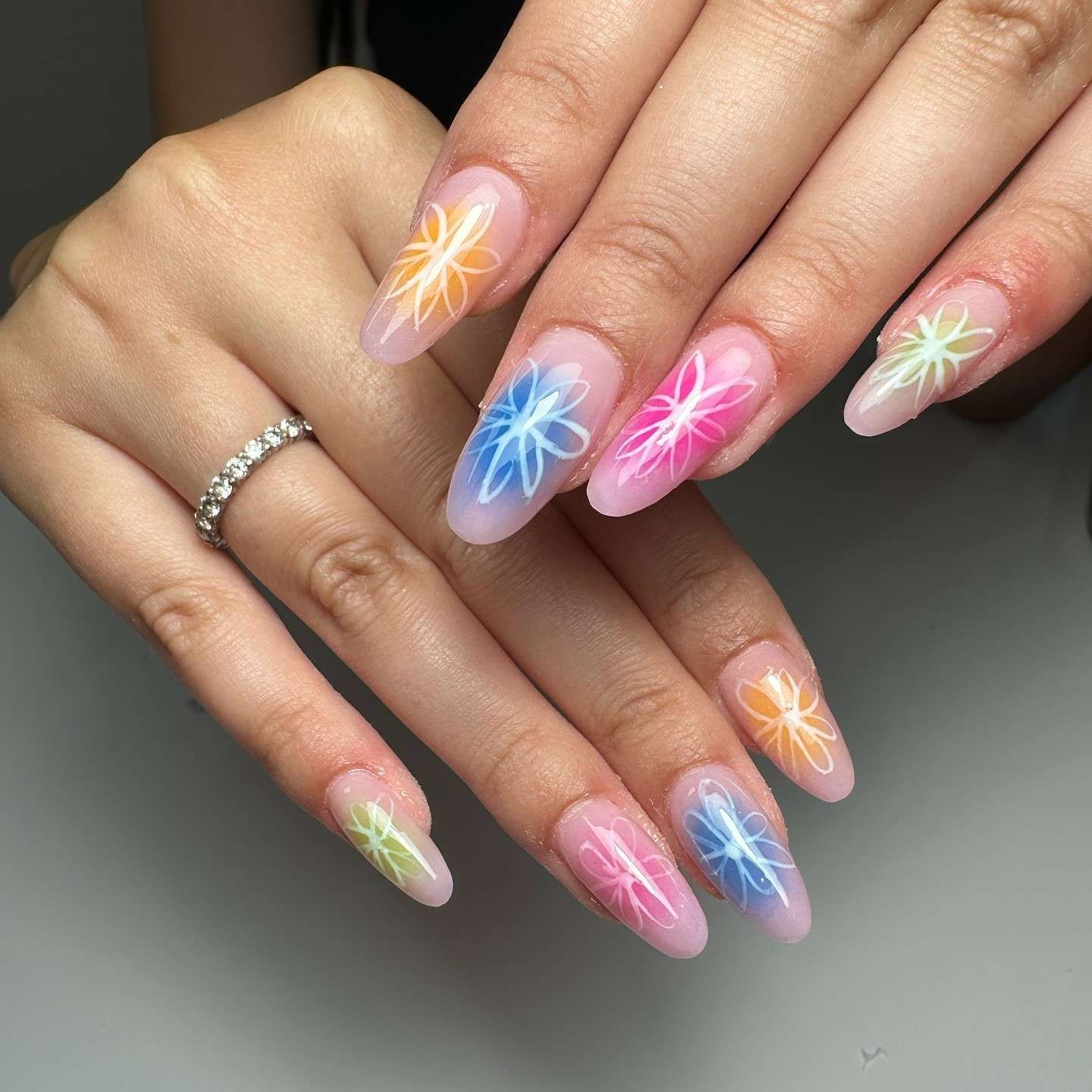 Mano con uñas largas y rosas bien cuidadas y detalles brillantes, apoyada sobre una superficie suave y peluda de color rosa.
