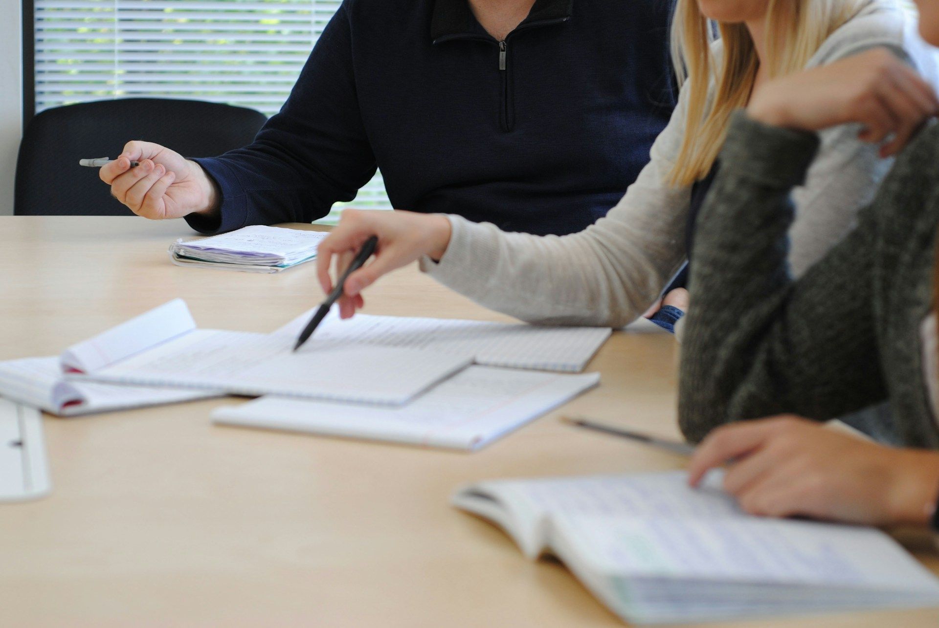 Des personnes assises à une table en réunion prennent des notes sur des feuilles avec des stylos.