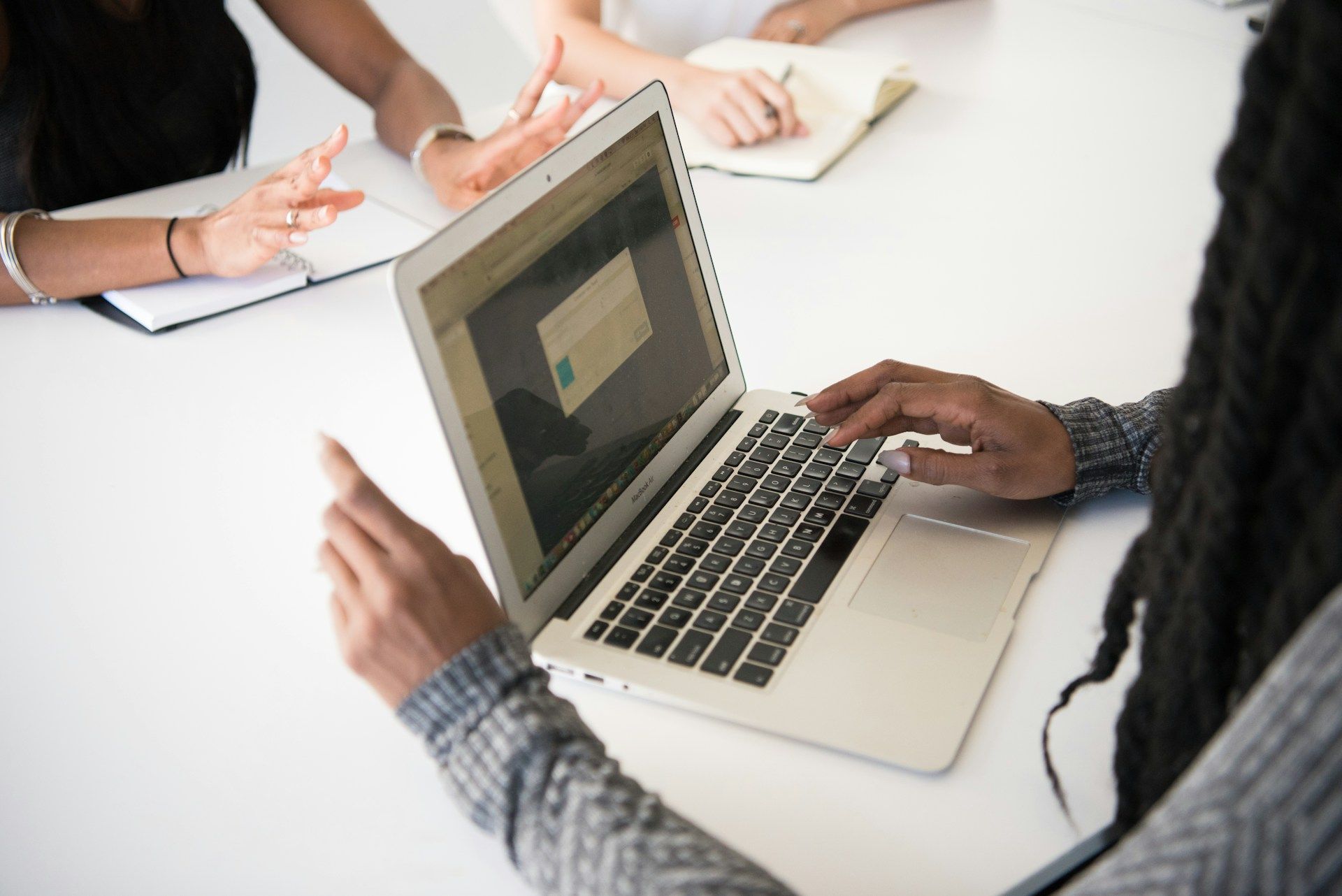 Des personnes collaborent autour d'un ordinateur portable à une table de réunion, leurs mains désignant des documents.