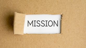 Une carte blanche portant l'inscription « MISSION » apparaît à travers un fond de papier brun déchiré.