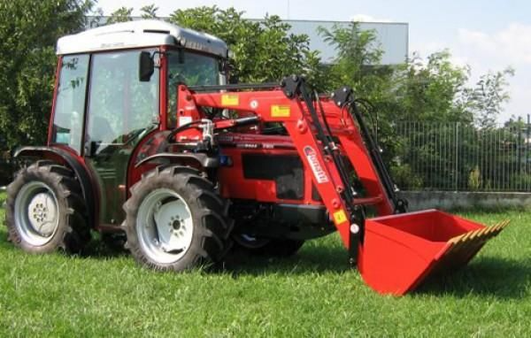 Un tractor rojo con un cubo rojo acoplado a él.