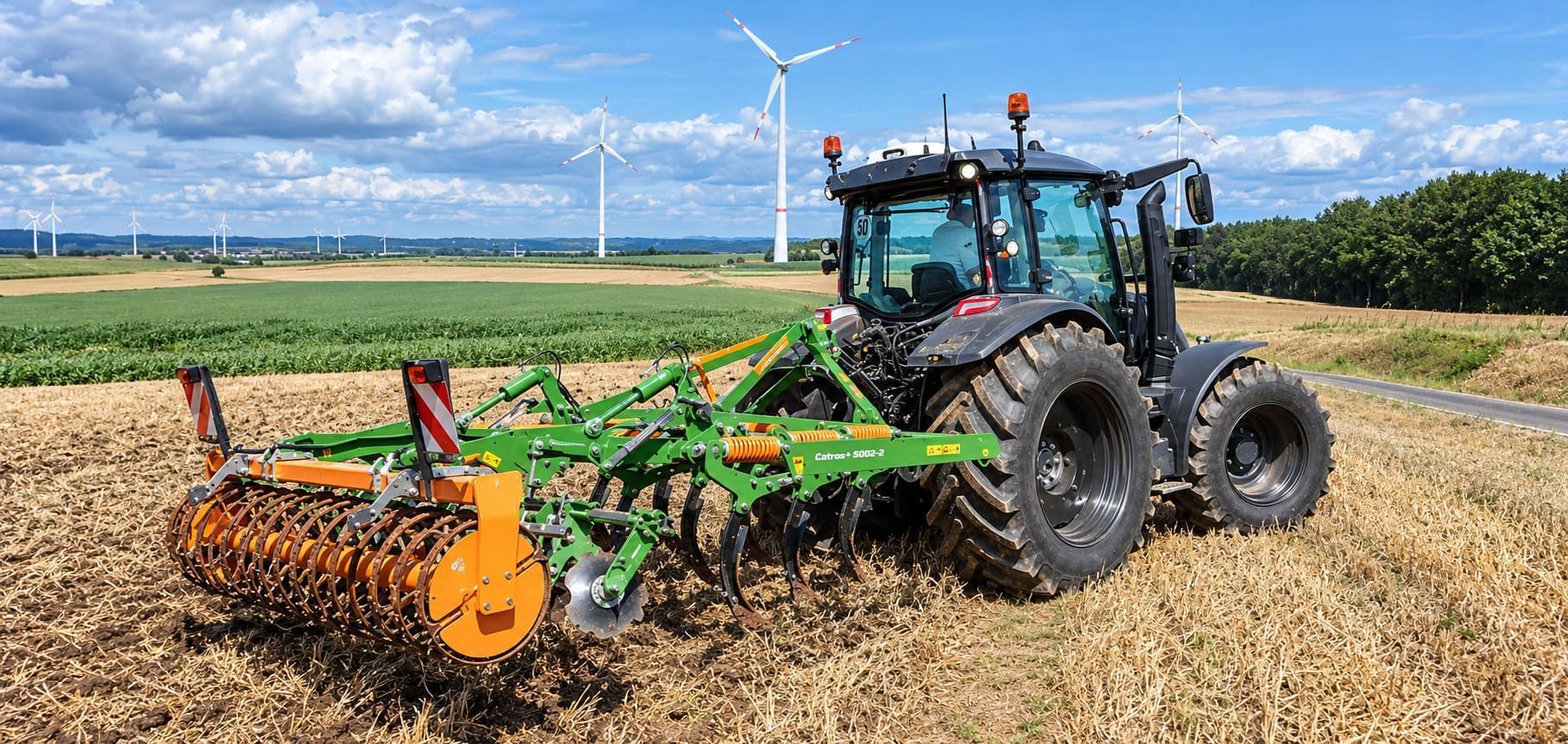 Tractor rojo arando un campo bajo un cielo azul con aerogeneradores al fondo.