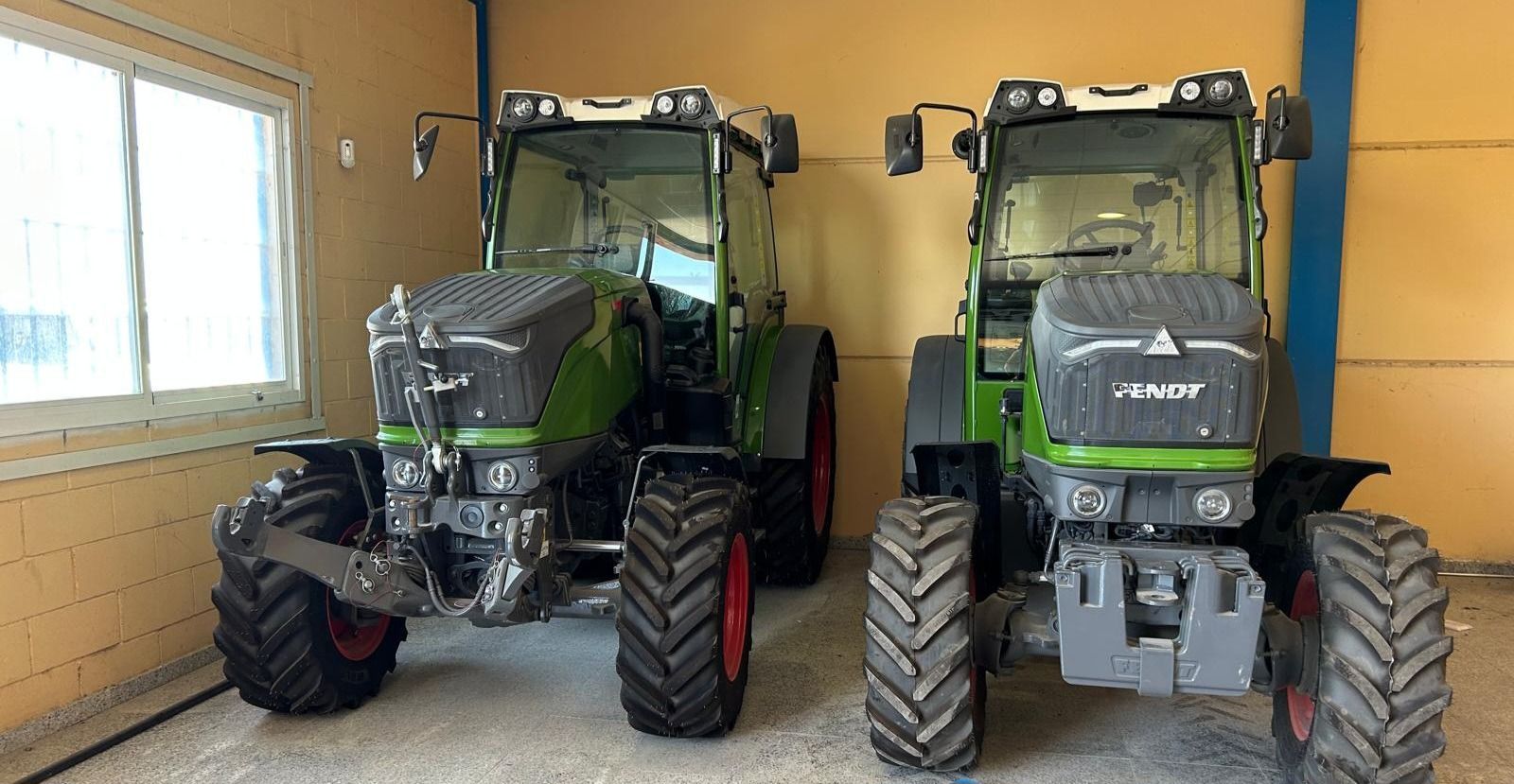 Dos tractores están estacionados uno al lado del otro en un garaje.