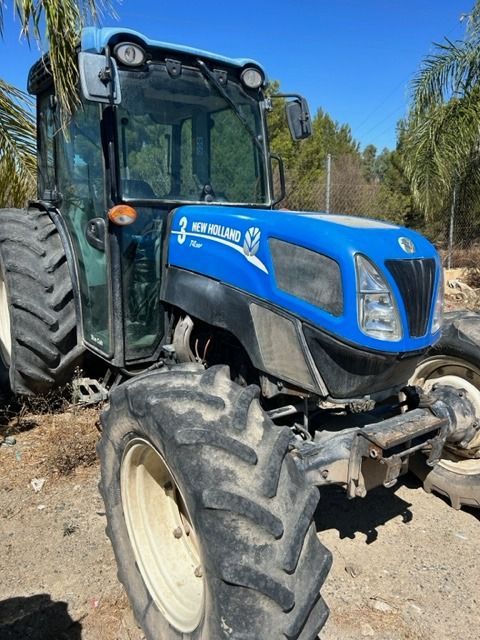 Un tractor New Holland azul está estacionado en el suelo.