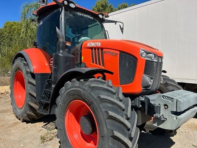 Un tractor rojo y negro está estacionado delante de un camión blanco.