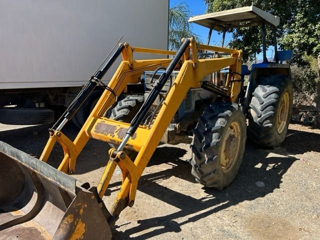 Un tractor amarillo con un cargador frontal está estacionado en un lote de tierra.