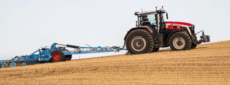 Un tractor rojo transporta maquinaria agrícola azul a través de un campo cosechado bajo un cielo despejado.